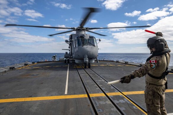 A member of the embarked Air Detachment onboard HMCS FREDERICTON provides signals to ensure safe cross deck operations with "GANCIO 05", a SH-101 helicopter from Italian Navy ITS MARGOTTINI during Operation REASSURANCE, on 19 February 2023 in the Mediterranean Sea.
