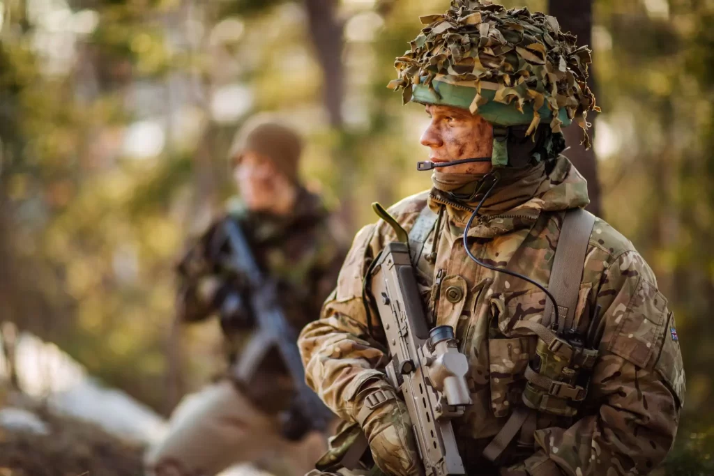 Two soldiers pause as they hike through a forest.